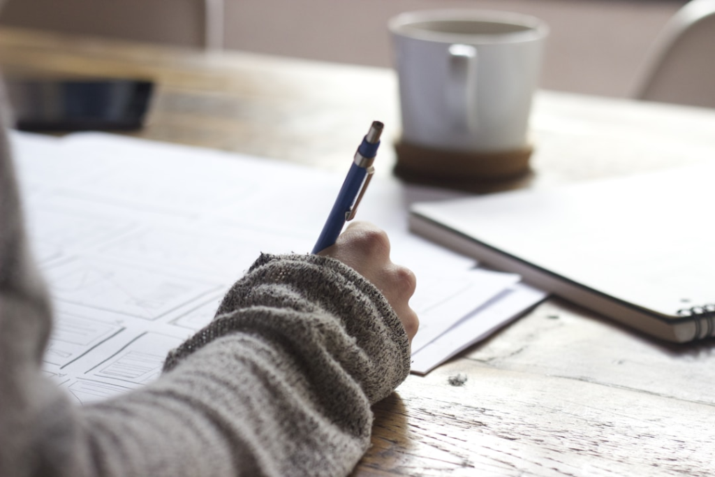 A person sitting at their work desk and writing out their plan for their newsletter before using a top newsletter software.