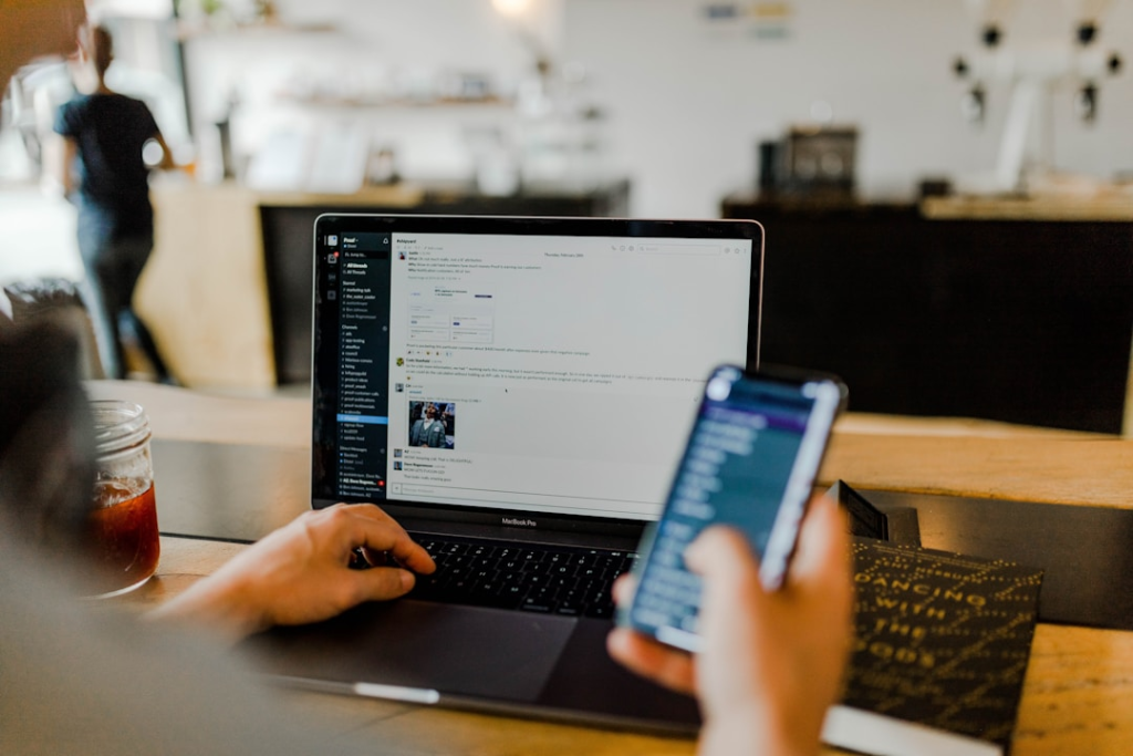 A person using their laptop and phone while they work on composing an email in a cafe.